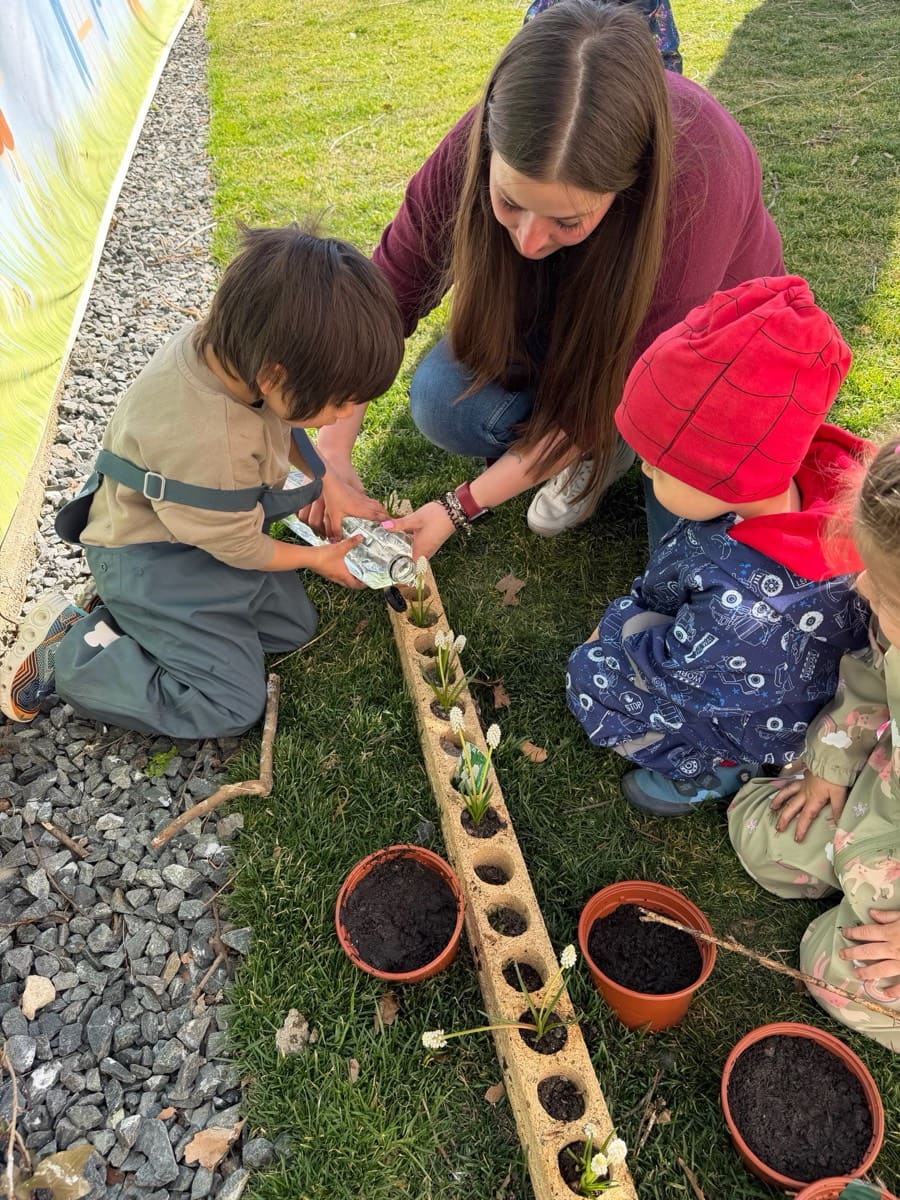 Copii și educatoare plantând flori în ghivece